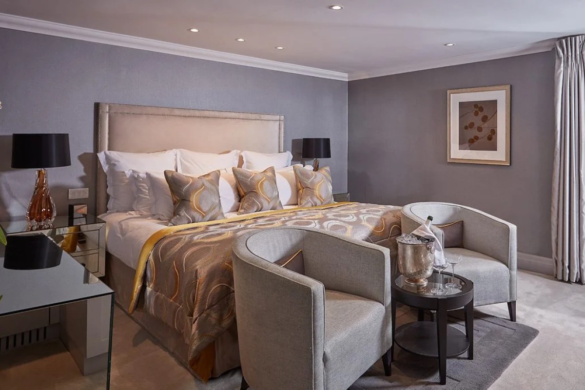Elegant hotel bedroom with grey upholstered bed, two armchairs and champagne bucket