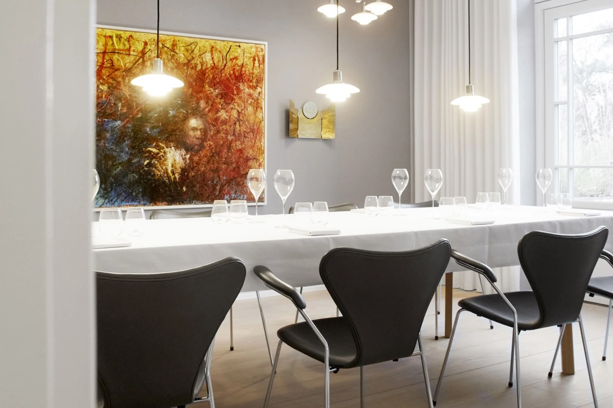 Elegant dining room with long white-clothed table, black chairs, and a large colorful painting on the wall.