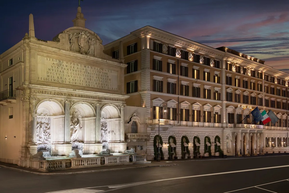 The St. Regis Rome building facade at dusk, illuminated with ornate fountain and Italian flag