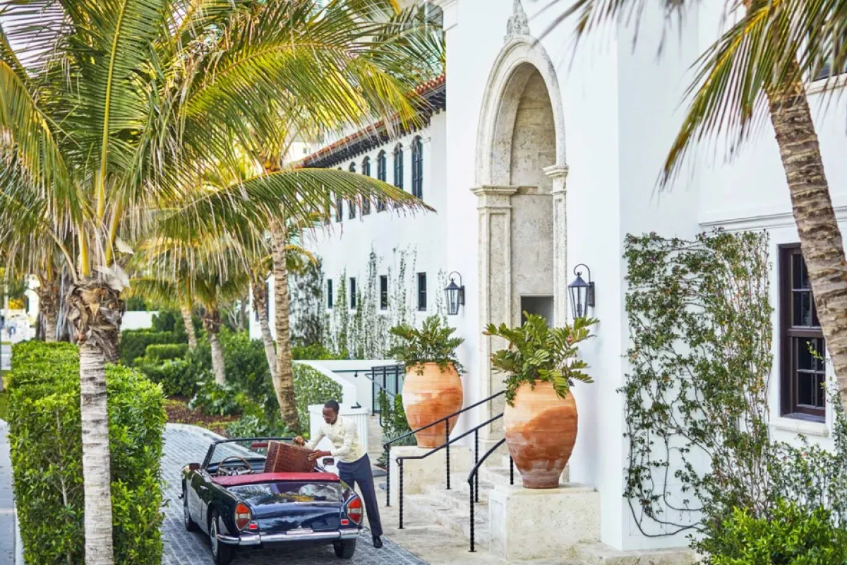 Exterior entrance of The Surf Club Restaurant with palm trees, vintage car and staff member assisting with luggage