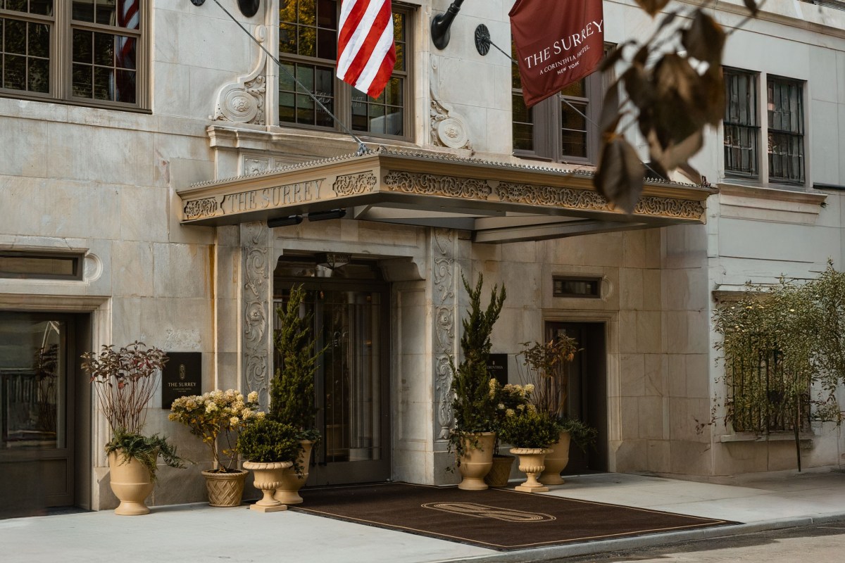 Street-level view of The Surrey hotel entrance with ornate stone facade, awning, flags, and potted plants.