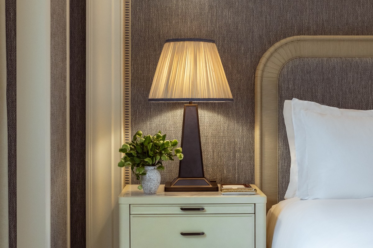Bedside table with lamp, plant and bed linens in guest room