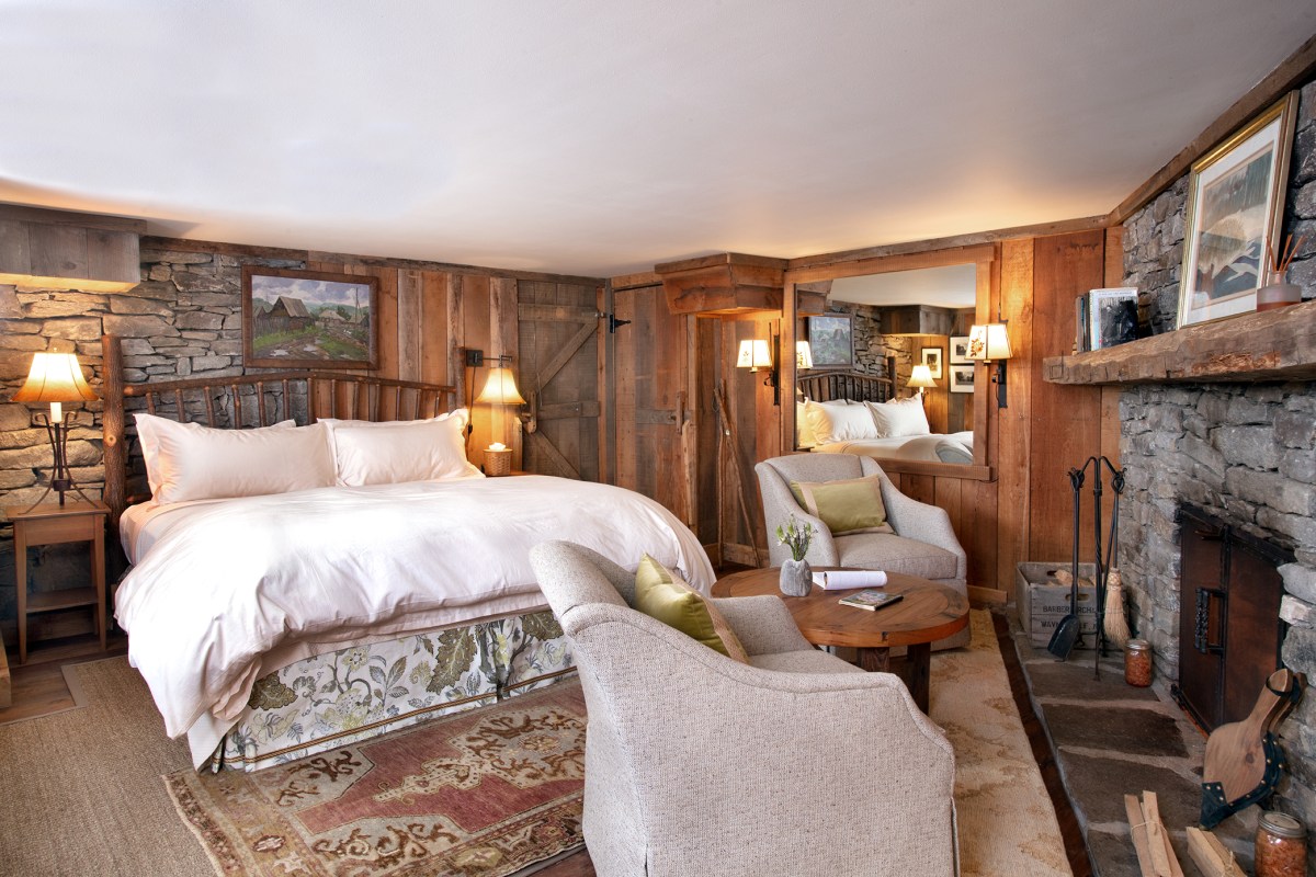 Rustic guest suite with a large bed, stone fireplace, and timber-paneled walls at The Swag.