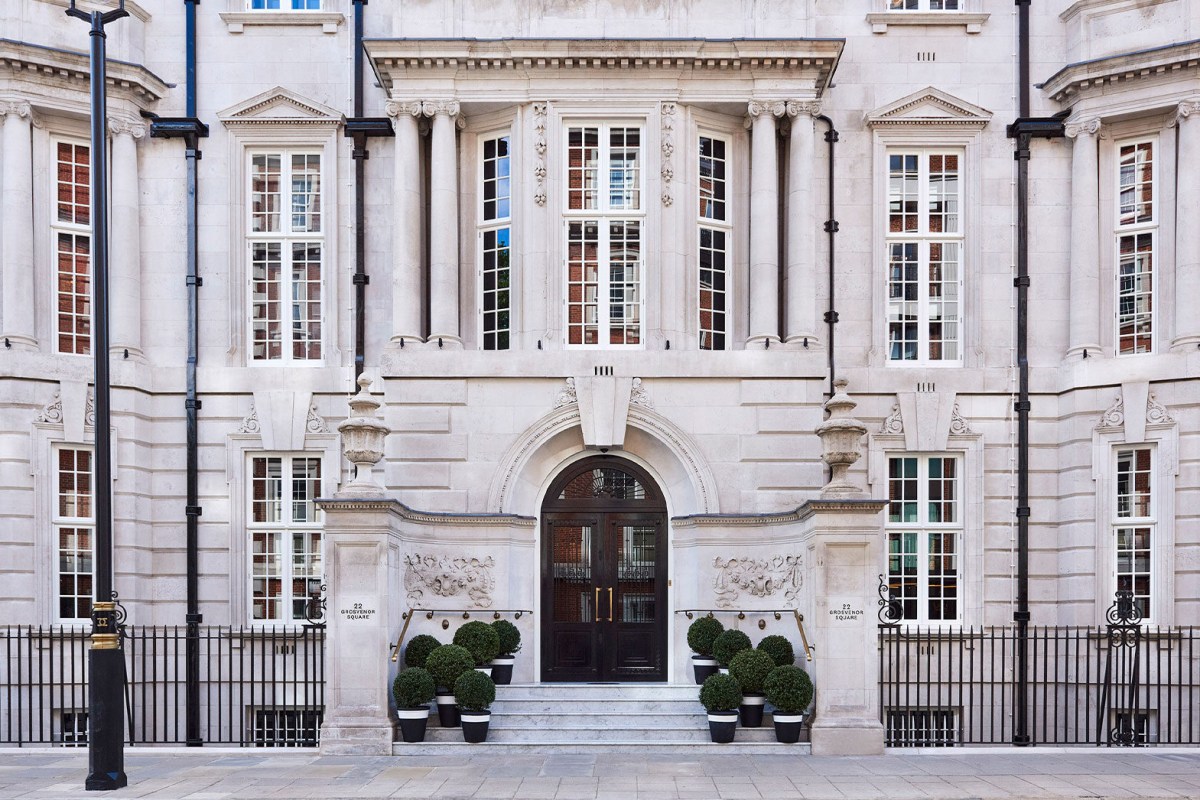 Elegant stone façade of The Twenty Two hotel with grand arched entrance, topiary planters and iron railings on Grosvenor Square