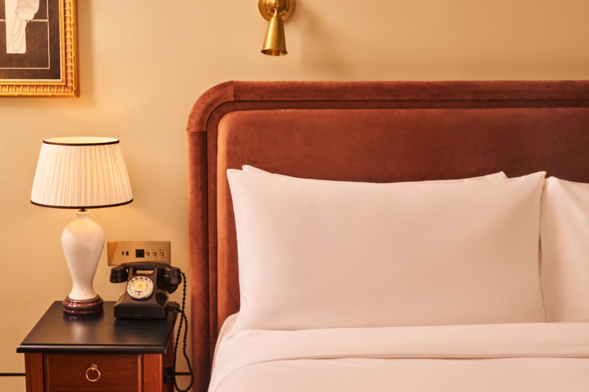 Guest room bed with velvet headboard, nightstand lamp and vintage rotary phone
