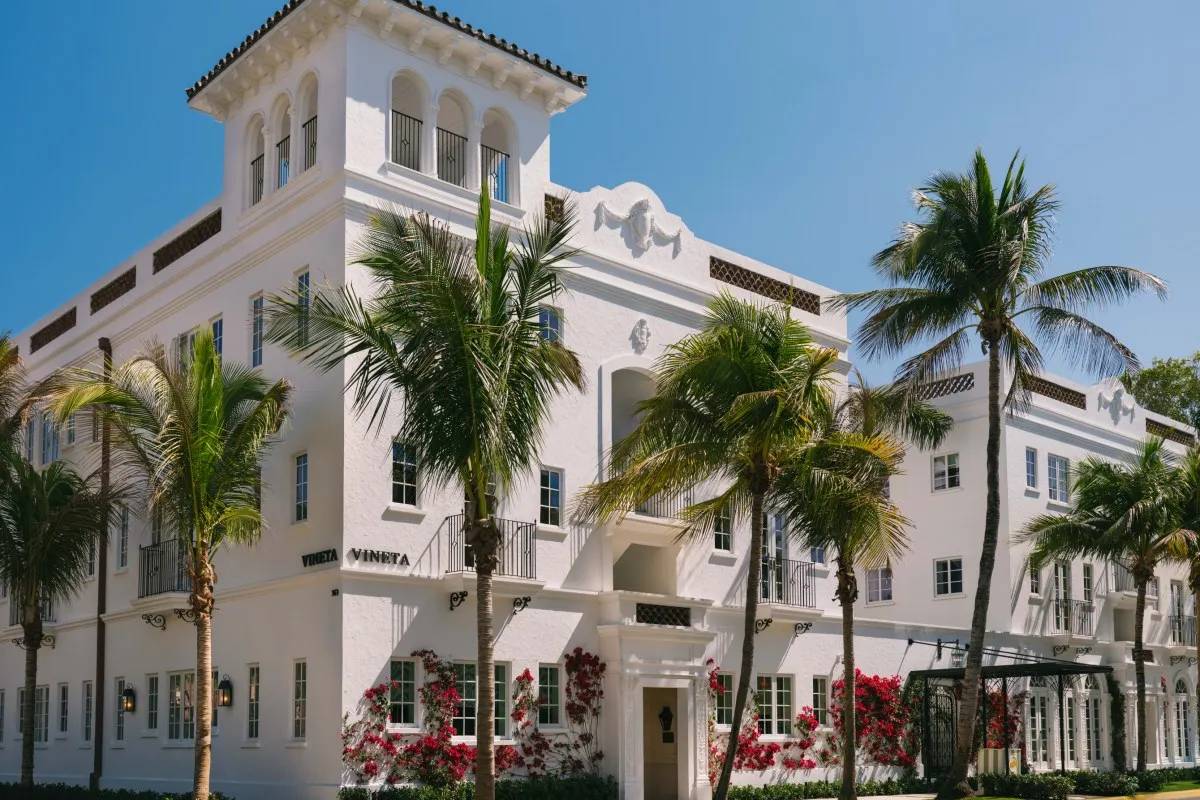 White Mediterranean-style hotel facade with tower, palm trees and red bougainvillea flowers, Vineta signage visible