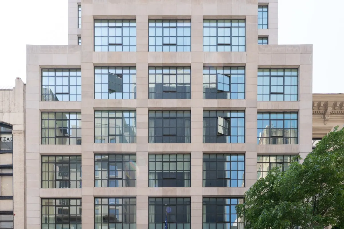 Street-level view of the stone façade of The Whitby Hotel showing grid windows and architectural detail, trees in foreground
