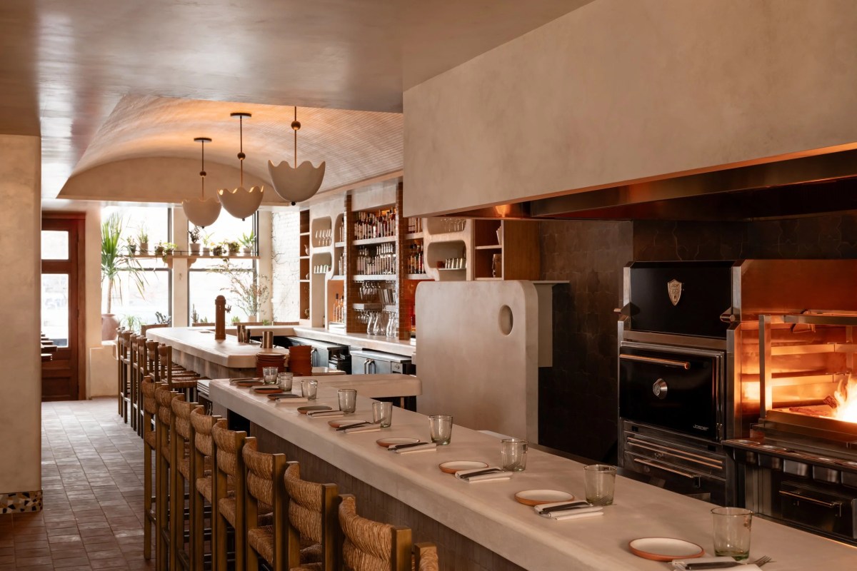 Restaurant interior with bar seating, wood-fired oven with open flame, and pendant lights