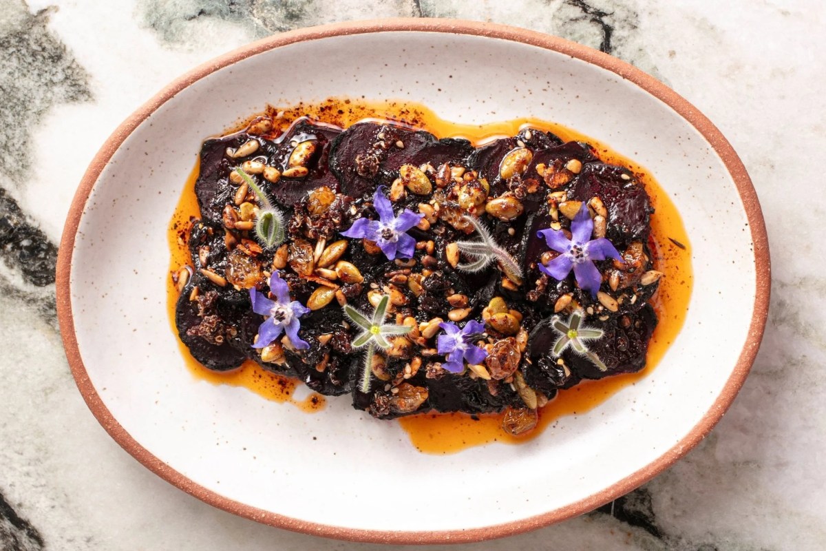 Plated roasted beets with seeds, chili oil, and purple edible flowers on marble