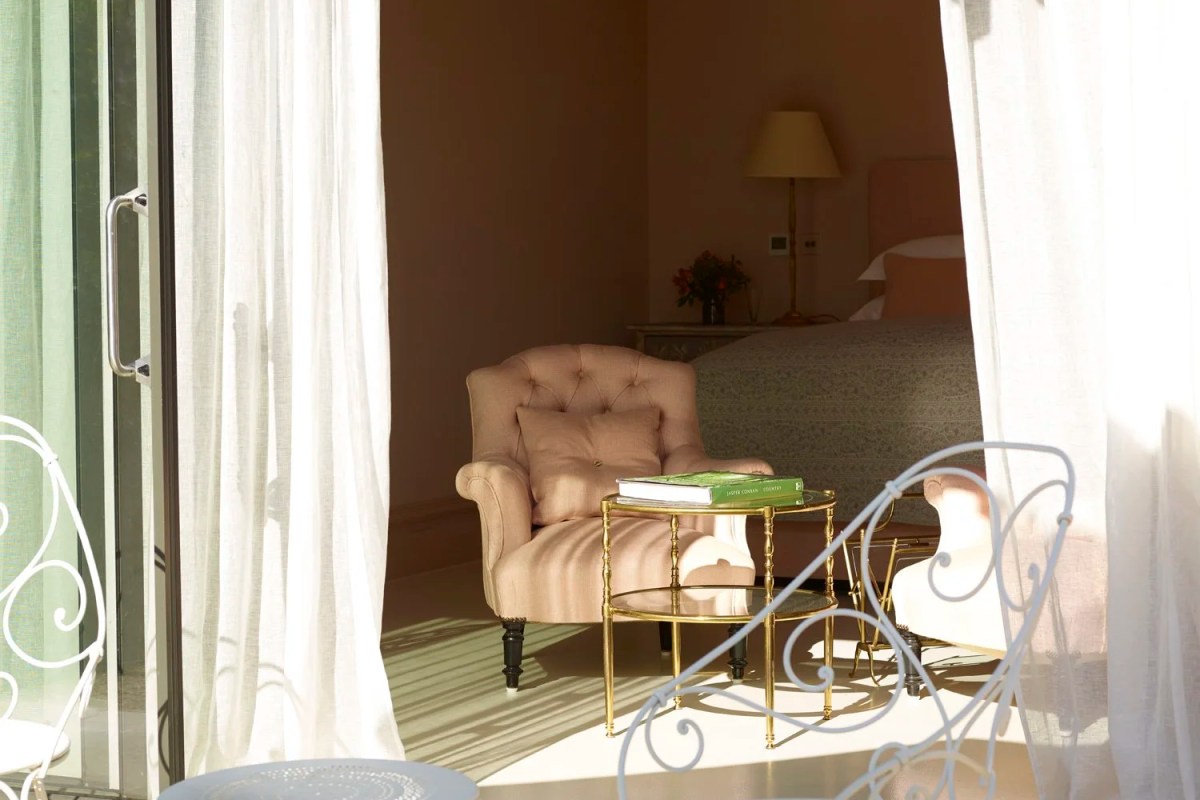 Elegant guest bedroom with pink armchair, gold side table and bed seen through sheer curtains