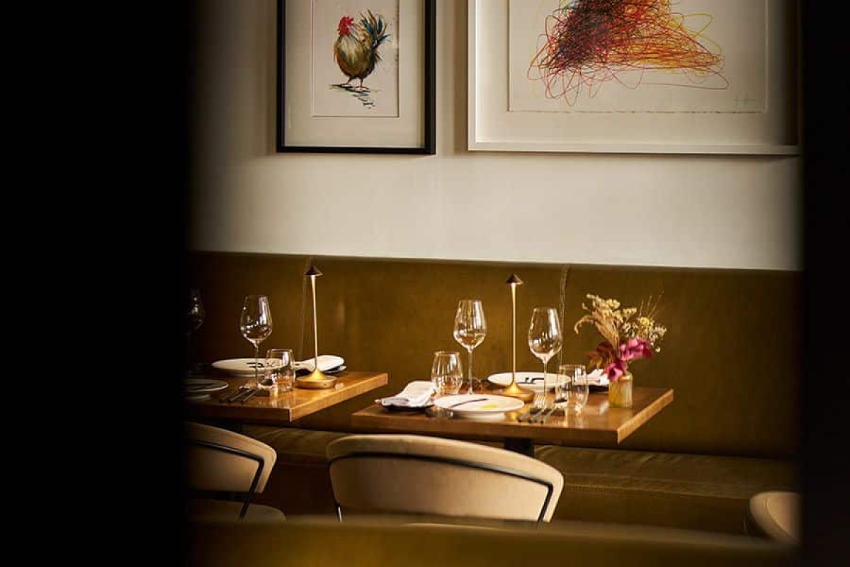 View through doorway into dining room with two set tables, banquette seating and framed art