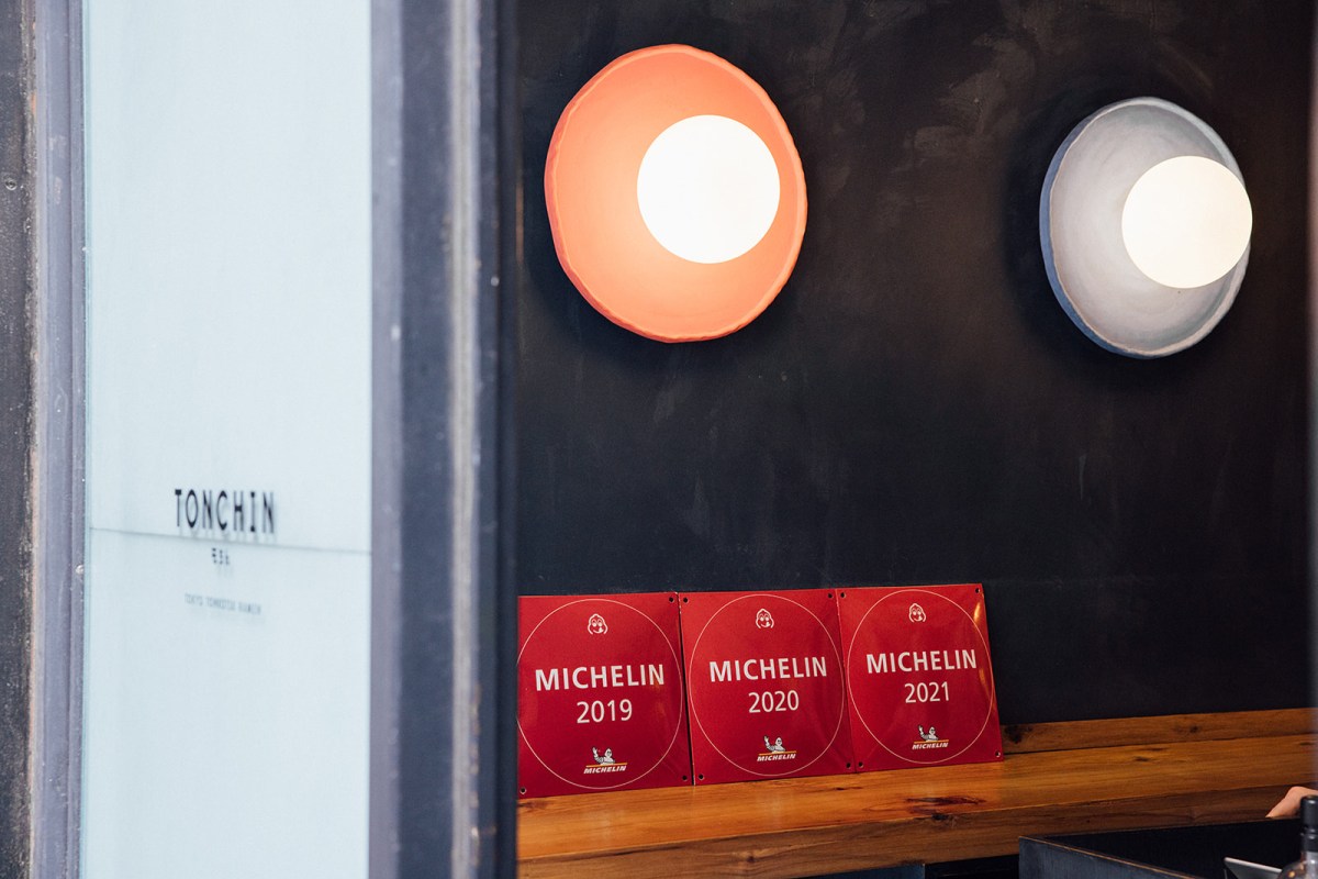 Close-up of the restaurant's entrance area showing the Tonchin sign, round wall lights, and three Michelin award plaques.