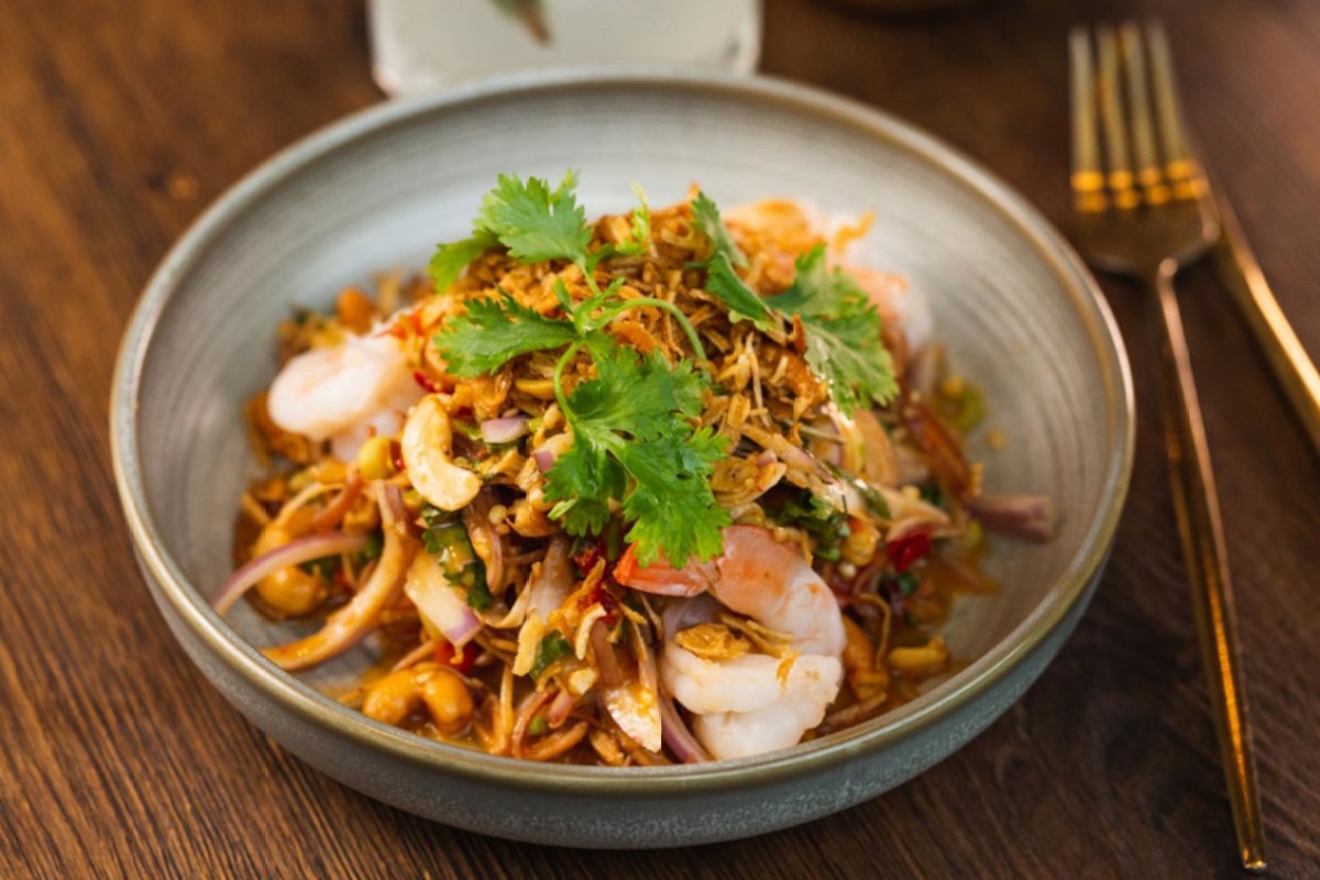 Bowl of Thai shrimp salad with crispy shallots and cilantro on a wooden table