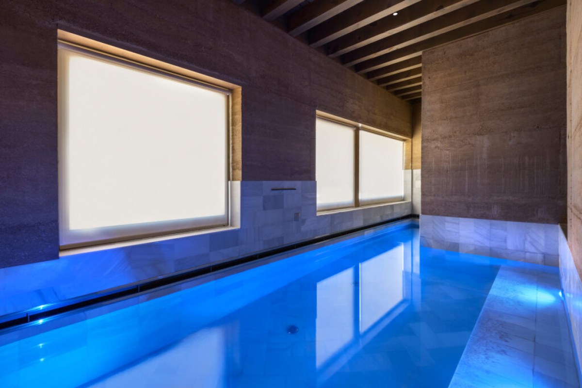 Indoor pool with blue lighting, stone walls, and wooden beamed ceiling