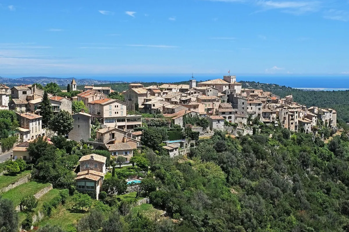 The stone village of Tourrettes-sur-Loup on its ridge above wooded slopes, with the sea on the horizon