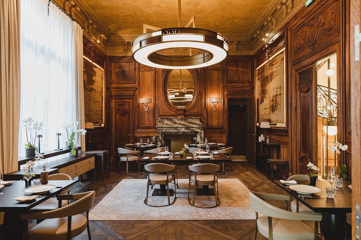 Elegant wood-paneled dining room at Trente-Trois with set tables, ornate fireplace, mirror and round pendant light.