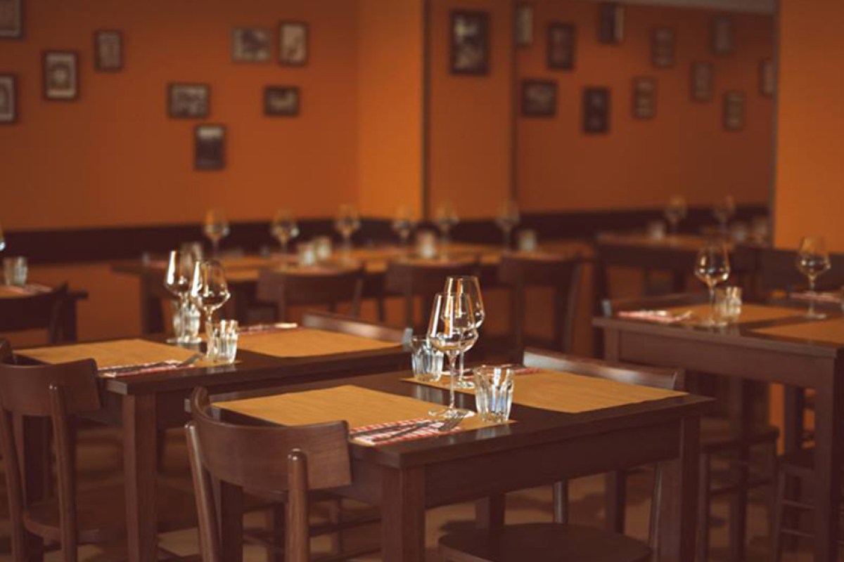 Dining room with orange walls, dark wood tables set with wine glasses and place settings