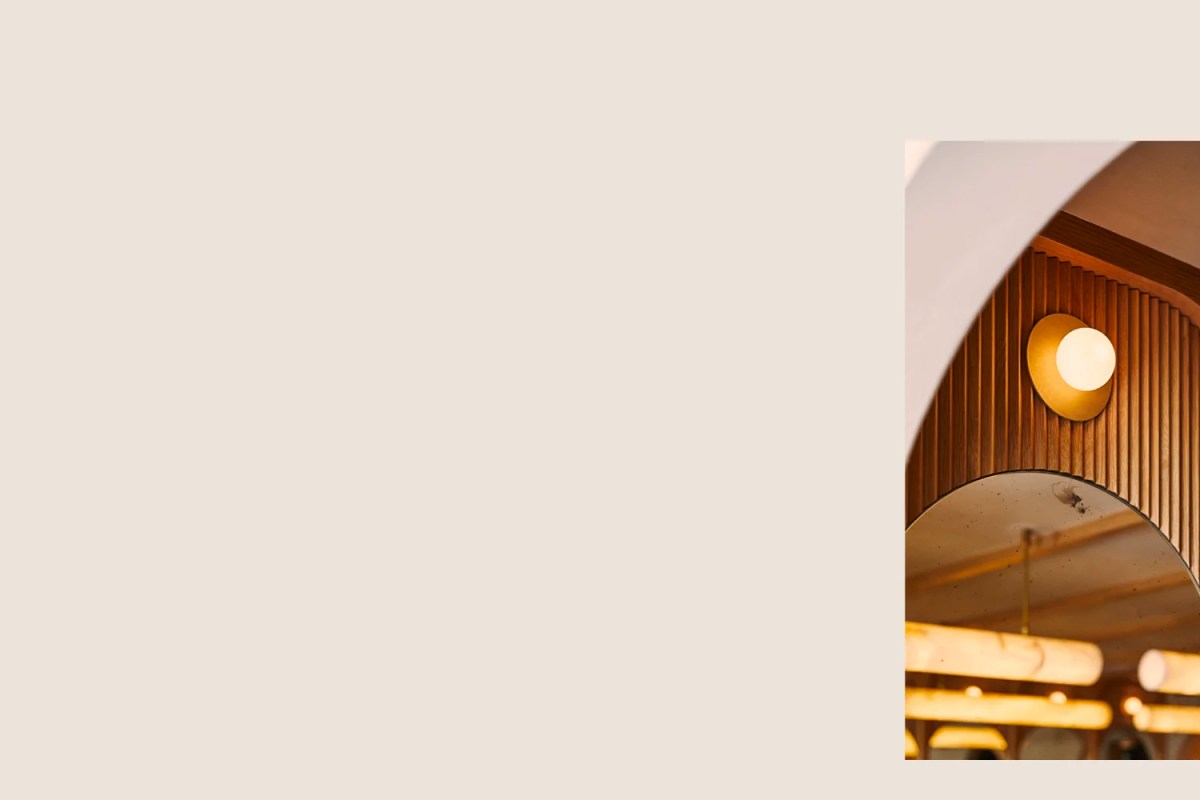 Close-up of an arched wood-paneled ceiling with a round brass wall sconce, part of the restaurant's dining room interior.