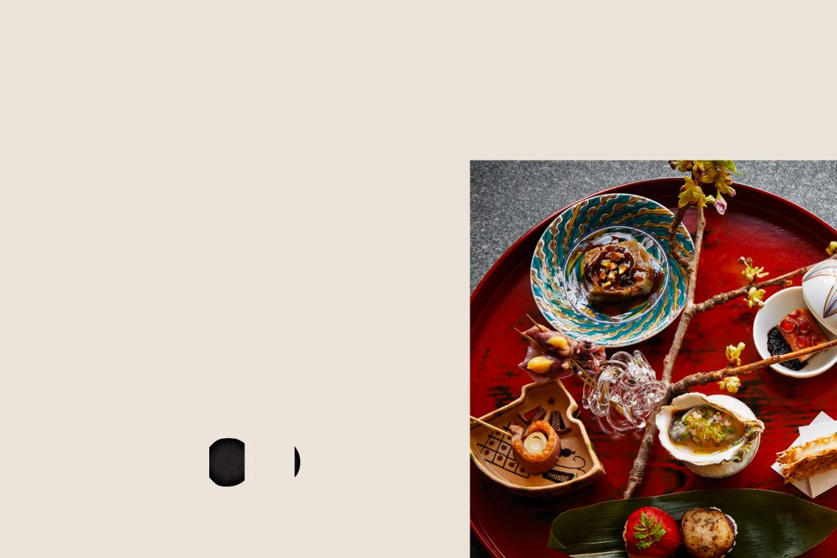 Elegant tray of Japanese-style dishes including seafood, meat skewers, and small bowls, artfully arranged with a cherry blossom branch.