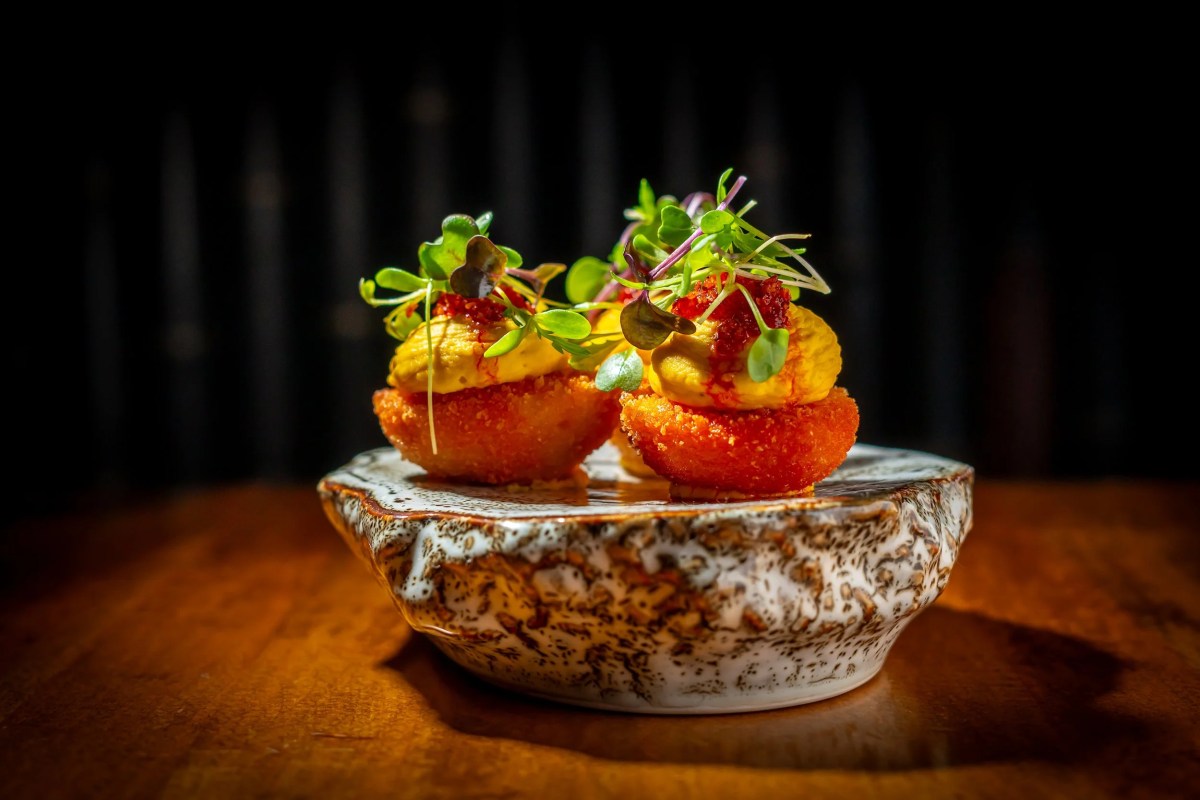 Crispy bites topped with yellow cream, red sauce, and microgreens served in a decorative bowl on a wooden table