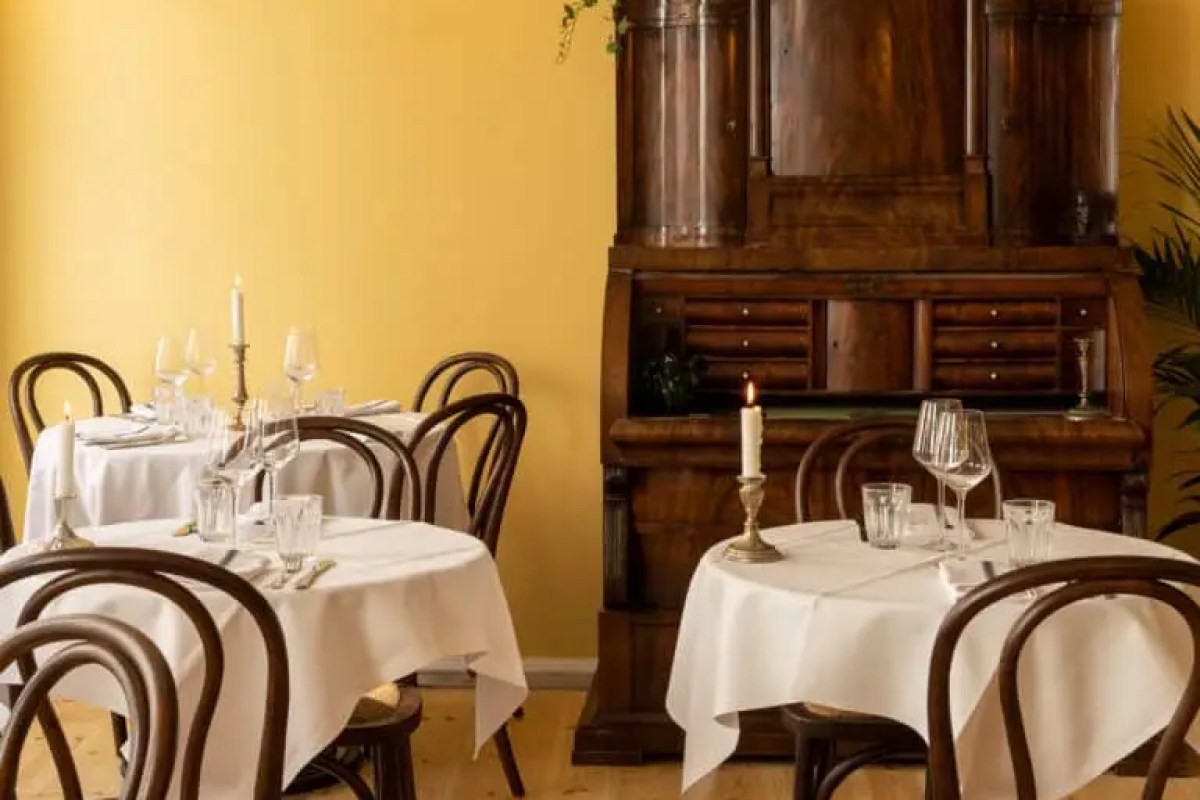 Elegant dining room with yellow walls, antique wooden cabinet, candlelit tables set with white linens and wine glasses