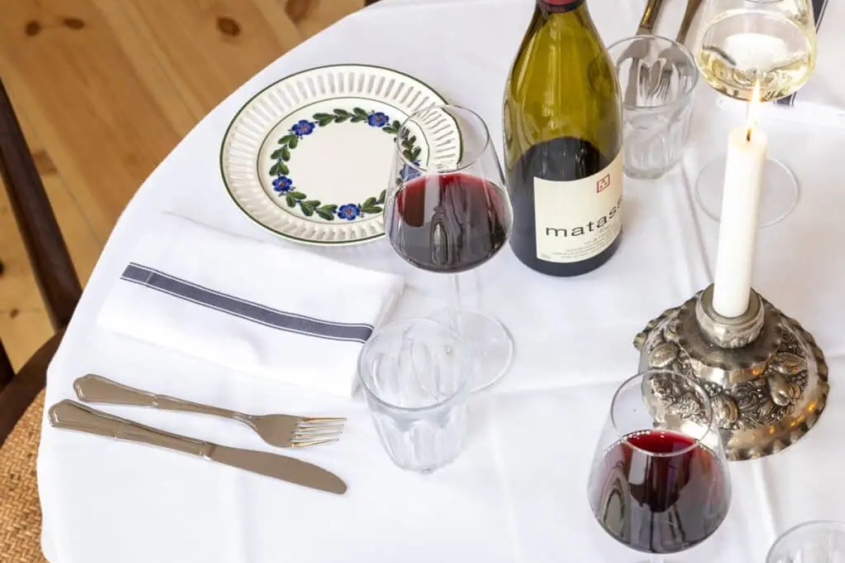 Overhead view of a laid restaurant table with wine glasses, a candle, cutlery, and a patterned plate on a white tablecloth