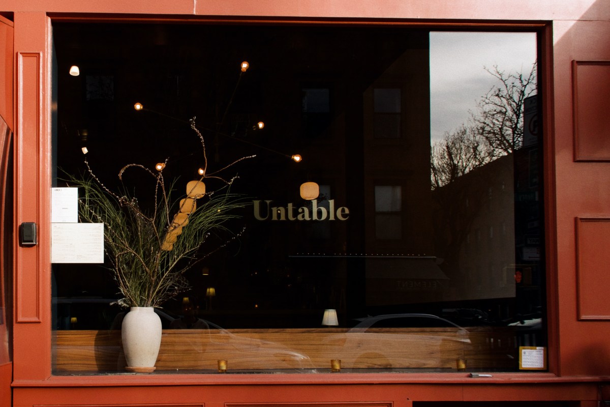 Untable restaurant storefront window with gold logo lettering and a vase of branches, red facade