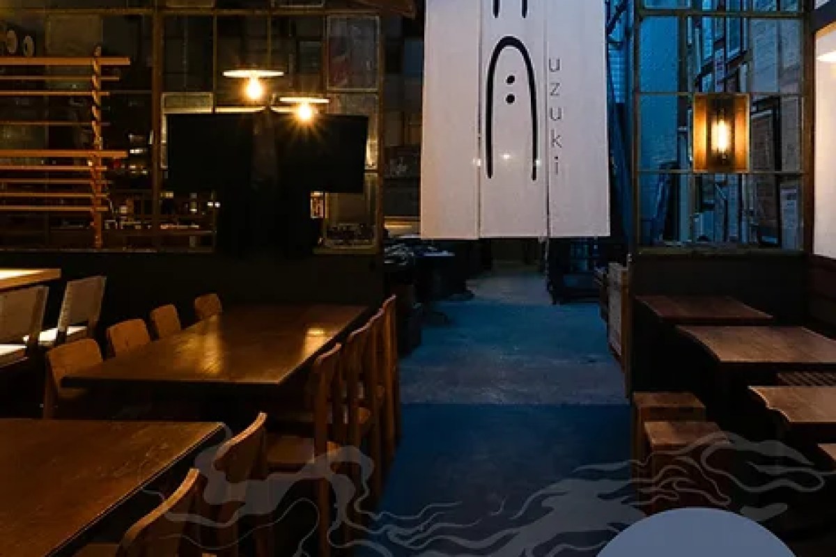 Interior of Uzuki restaurant showing dining tables, chairs, and a noren curtain with the Uzuki logo