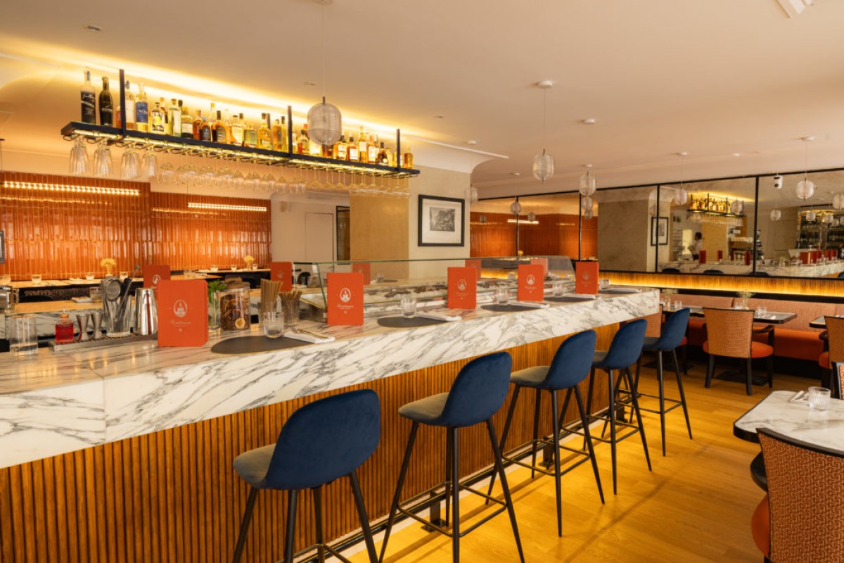 Wide view of restaurant interior showing bar seating, dining tables, and orange tiled backdrop