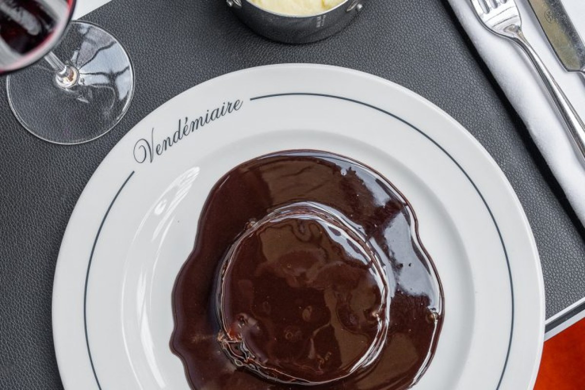 Chocolate dessert on a white plate with 'Vendémiaire' branding, alongside red wine and cutlery