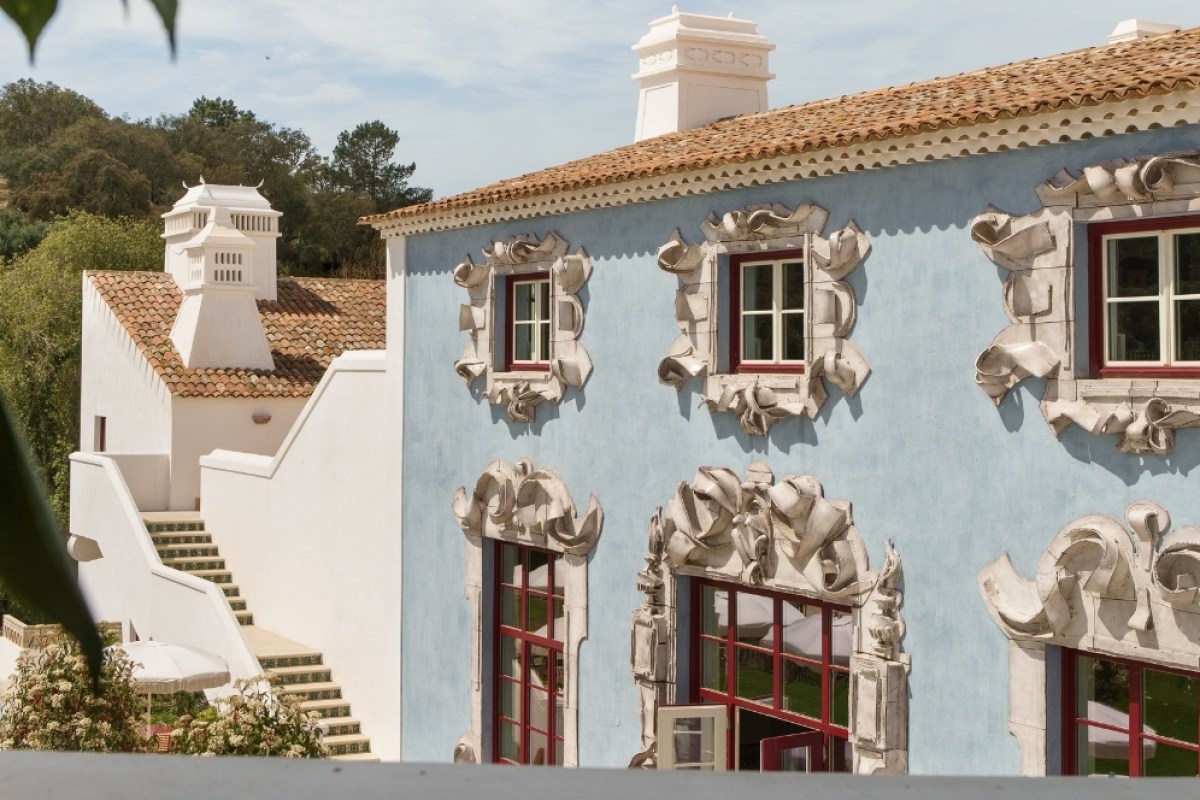 Pastel blue hotel façade with ornate white stucco window frames, chimneys and staircase.