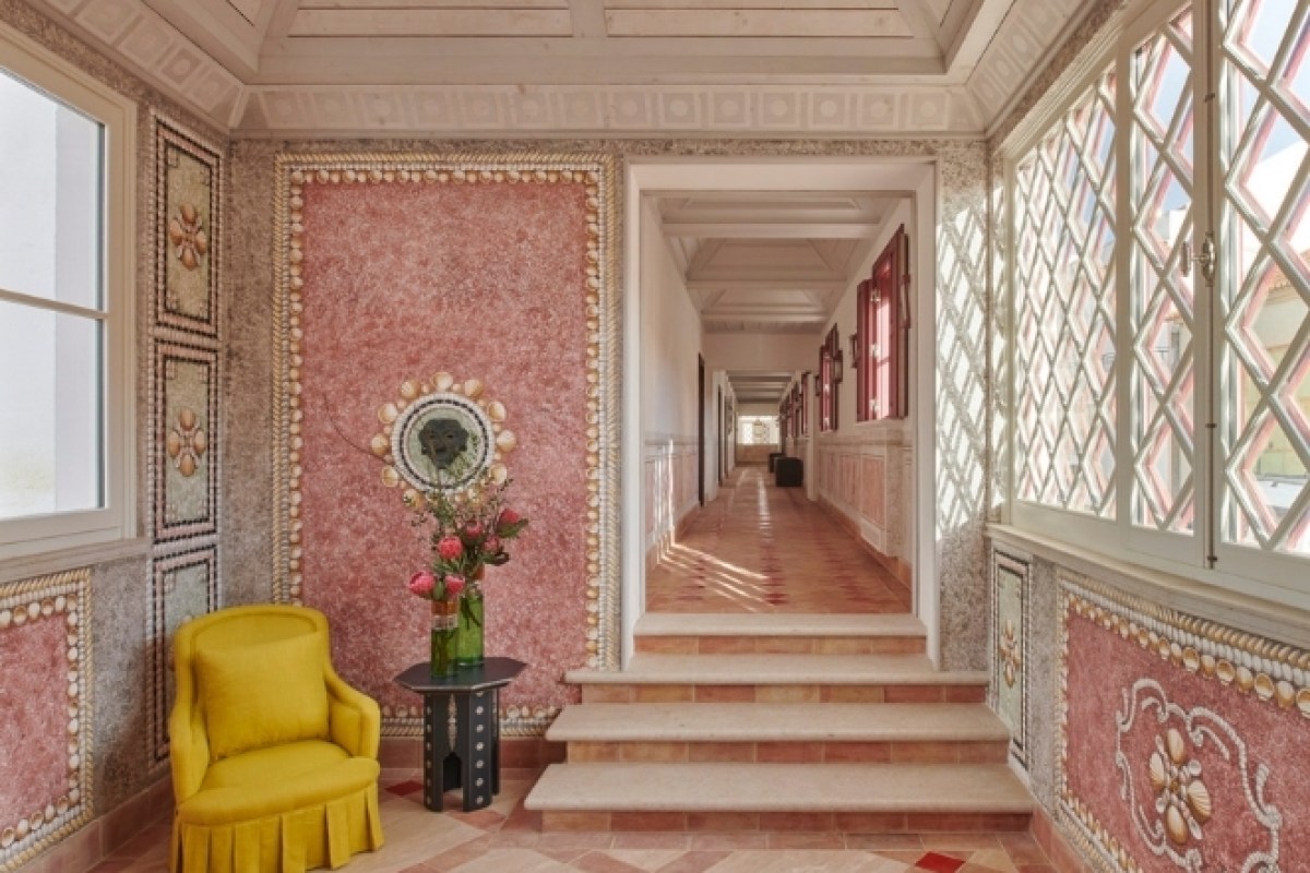 Hallway with pink shell-decorated walls, yellow armchair, and view down corridor