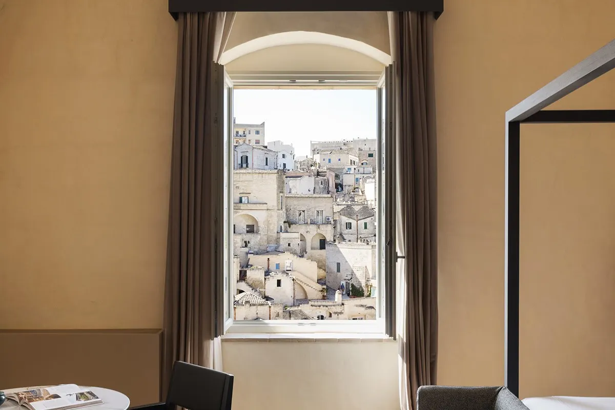 Guest room window with curtains framing a view over Matera's historic rooftops