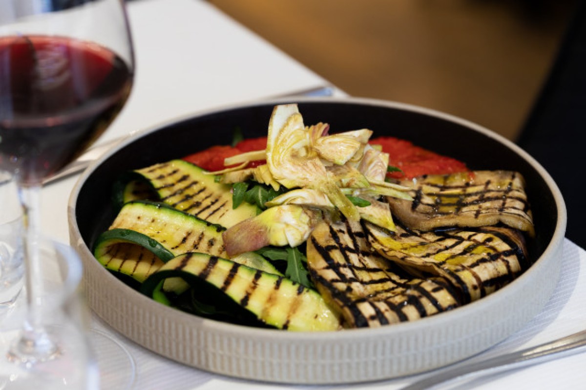 Grilled zucchini, eggplant and artichoke salad on a black plate with wine glass