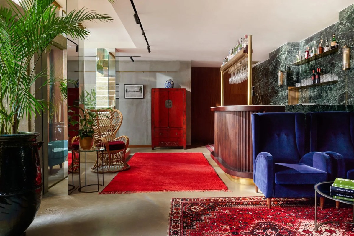 Hotel lounge and bar with blue velvet sofa, red Persian rugs, vintage red cabinet, and green marble bar