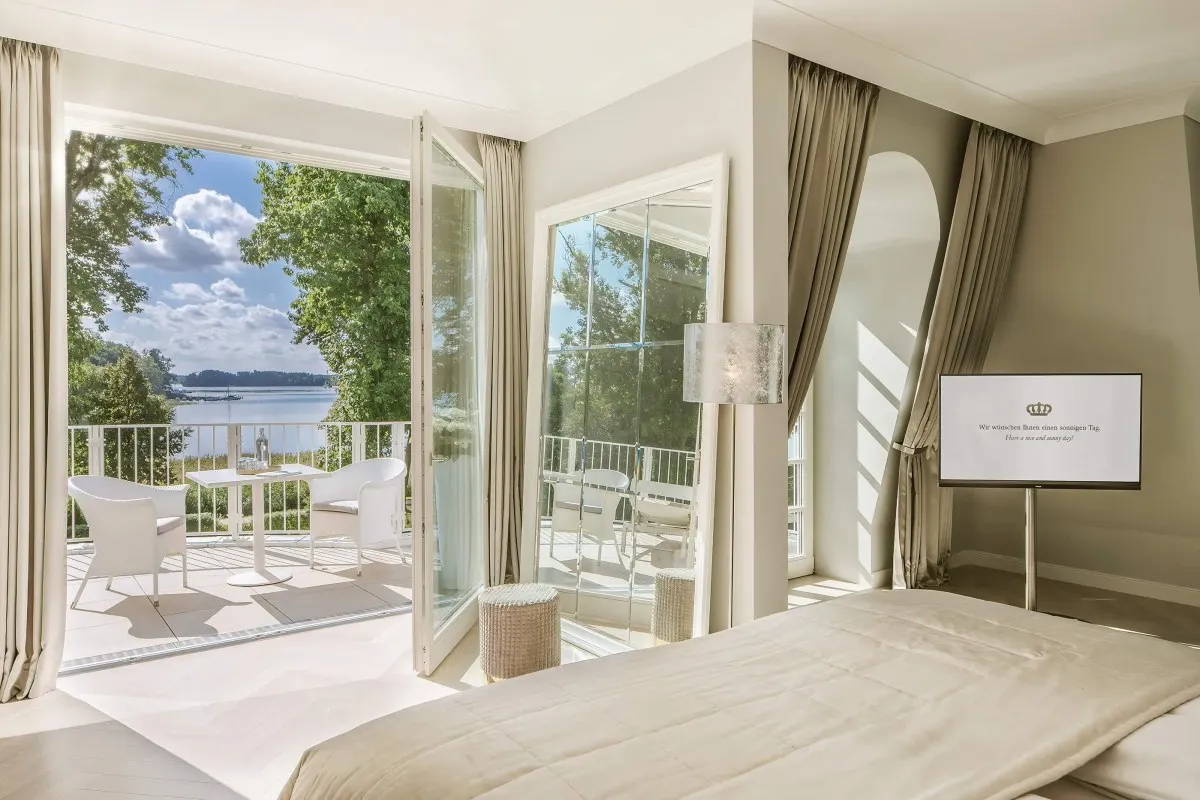 Elegant hotel guest room with bed, mirror, and open balcony doors showing lake view