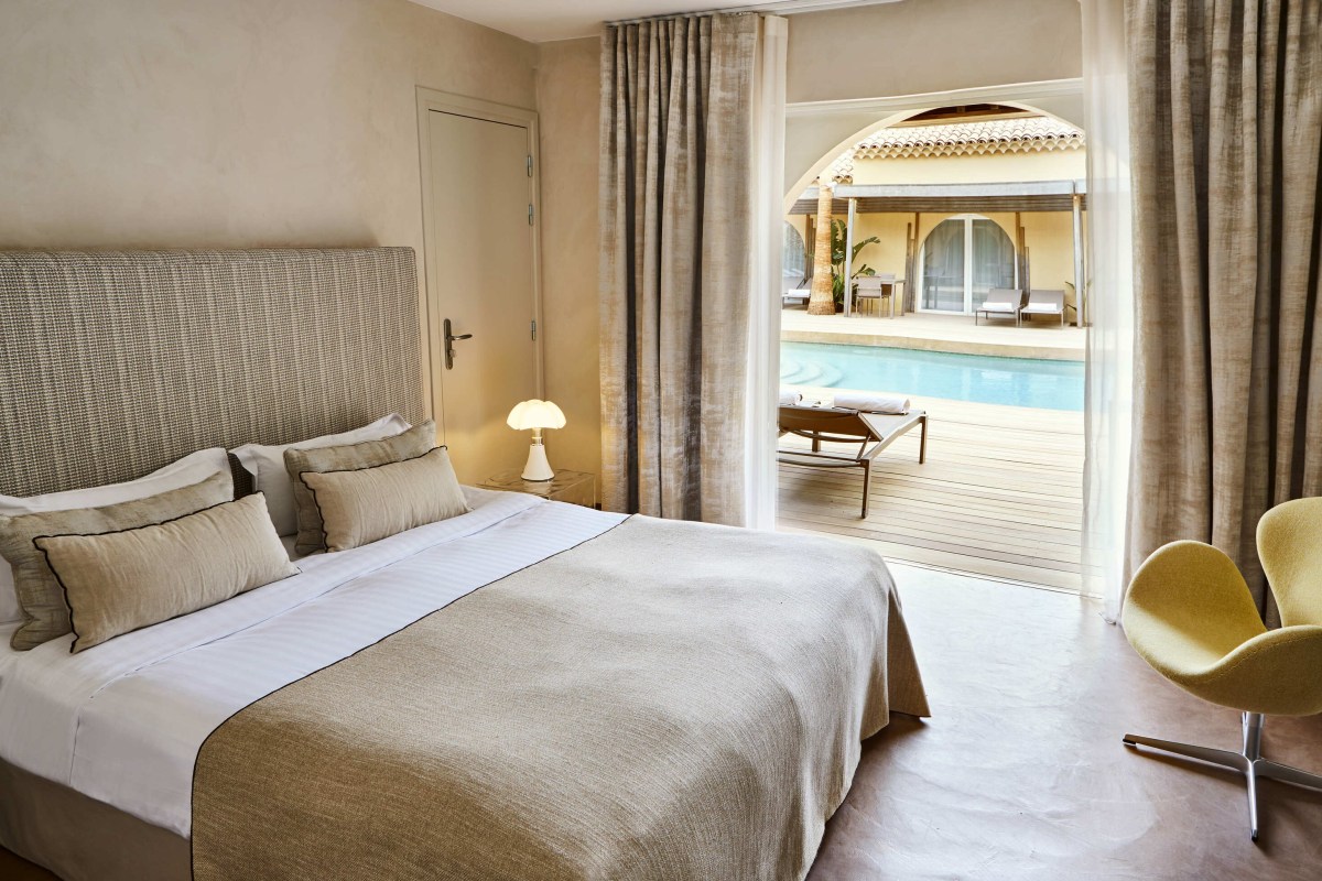 Elegant guest room with king bed, neutral linens, and doors opening to the pool terrace
