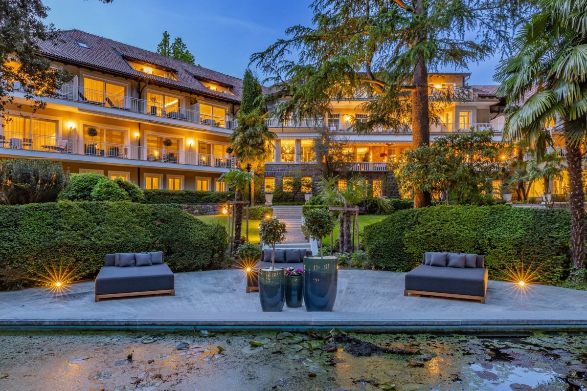 Villa Eden hotel exterior at dusk, illuminated facade with balconies seen across garden and pool terrace with loungers