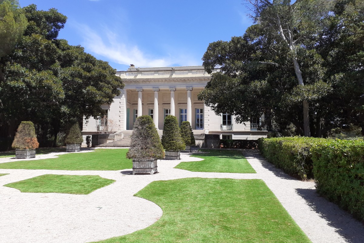 Villa Eilenroc on Cap d'Antibes seen across its formal garden, with lawns, gravel paths, clipped shrubs in planters and the colonnaded façade among the trees