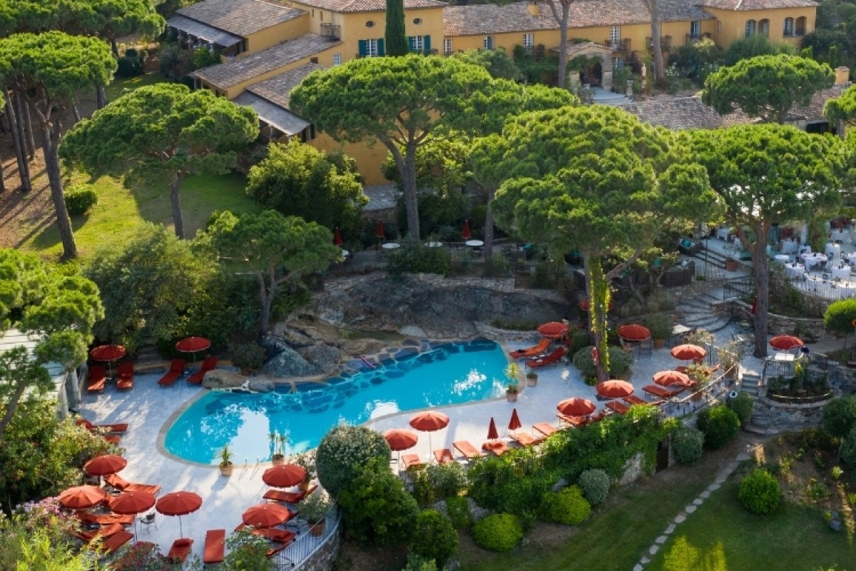Aerial view of hotel building with terracotta roofs, pool area, and dining terrace among pines