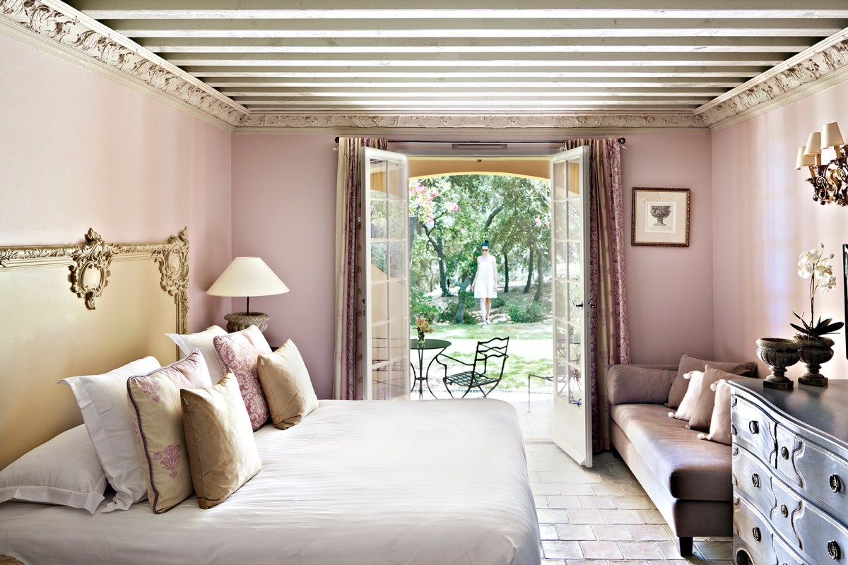 Elegant pink bedroom with ornate headboard, sofa, and doors opening to garden