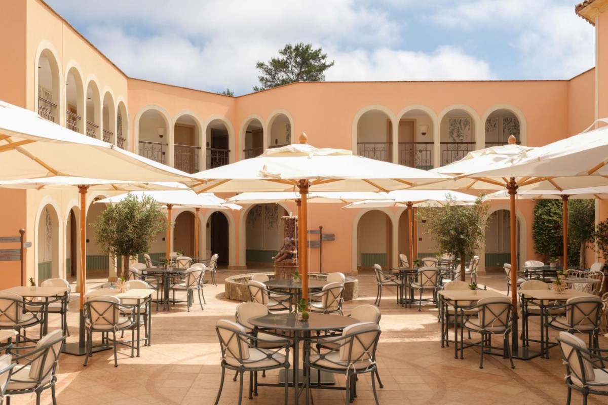 Courtyard of the hotel with cream umbrellas, dining tables, arched colonnade and fountain