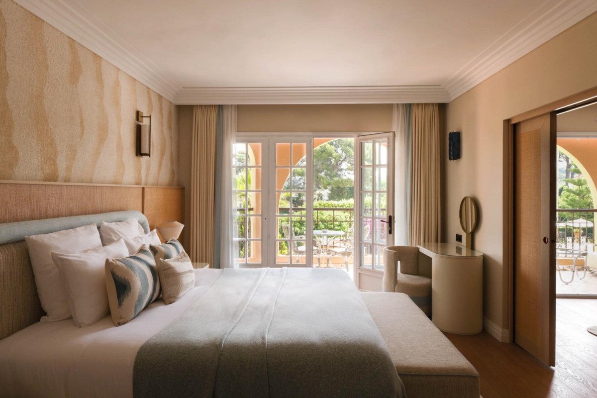 Bedroom with bed, desk and open French doors leading to terrace and garden view