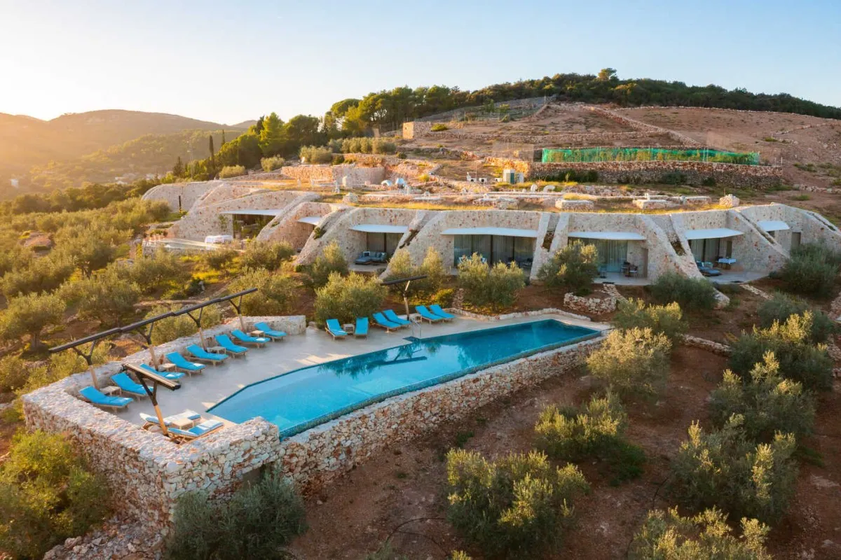 Aerial view of Villa Nai 3.3's stone building with grass-roofed terraces and infinity pool surrounded by olive trees