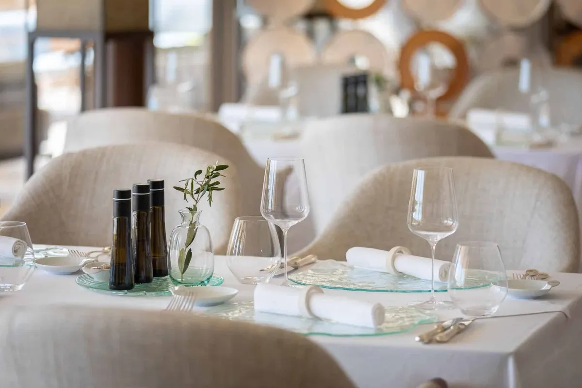 Elegant restaurant interior with set tables, wine glasses, and olive branch decor