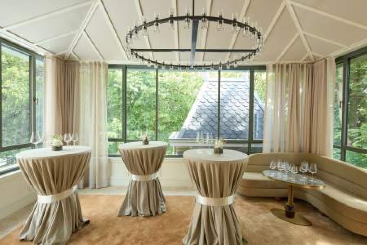 Elegant indoor lounge space with draped cocktail tables, chandelier, and garden view through tall windows