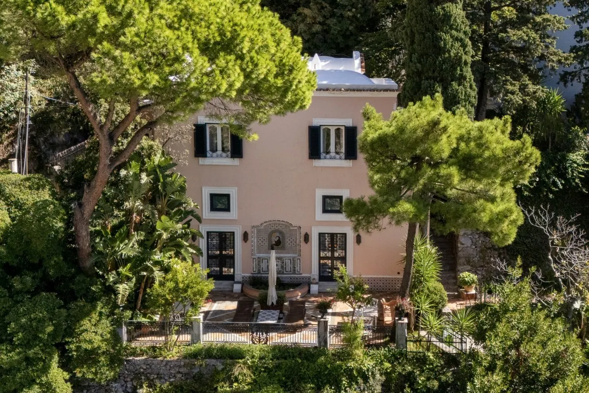 Aerial view of the pink Villa Treville building surrounded by lush pine trees and gardens overlooking the coast.