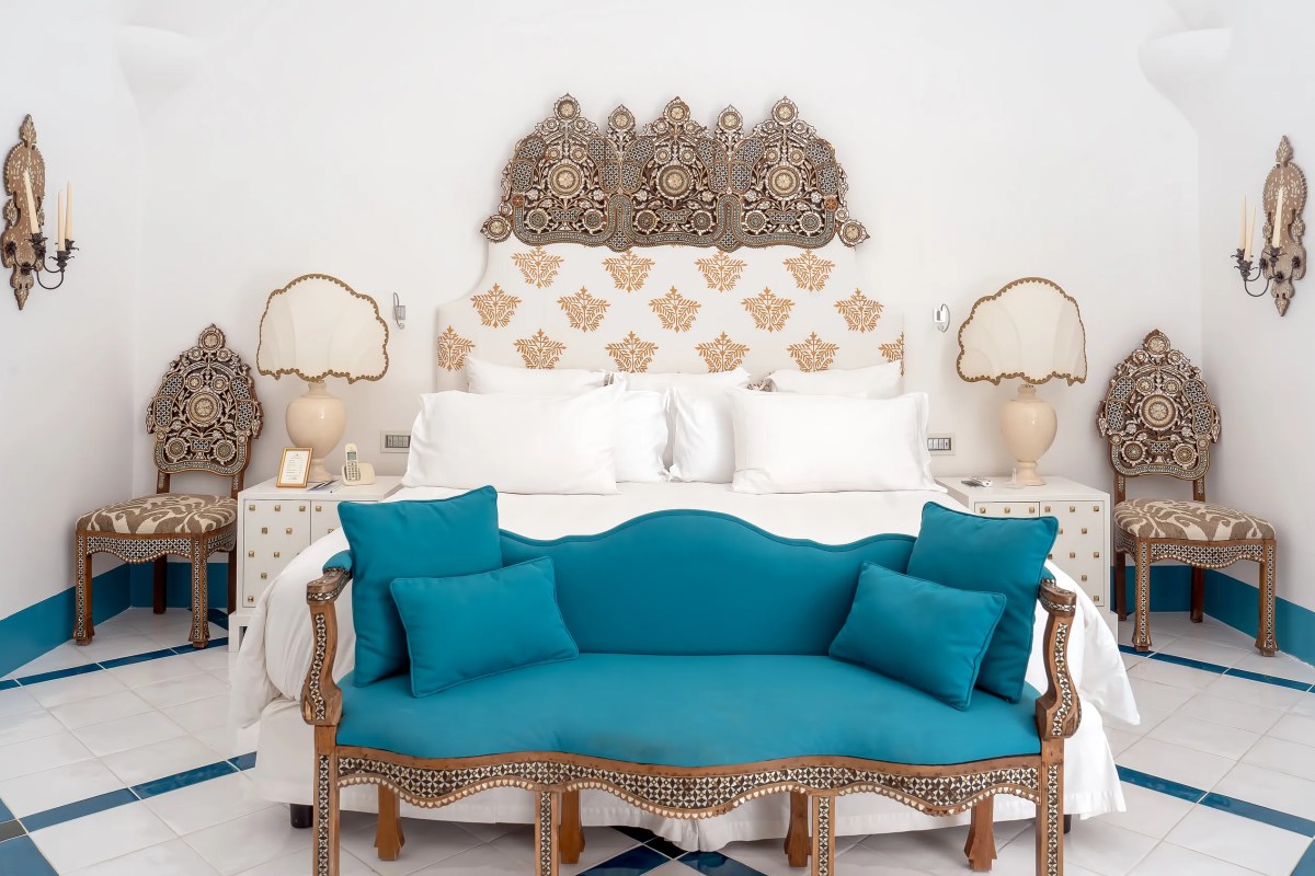 Guest suite with ornate inlaid headboard, teal sofa and patterned tile floor