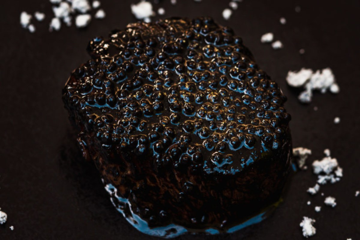 Close-up of a dark, glossy charred dish with salt flakes on black background
