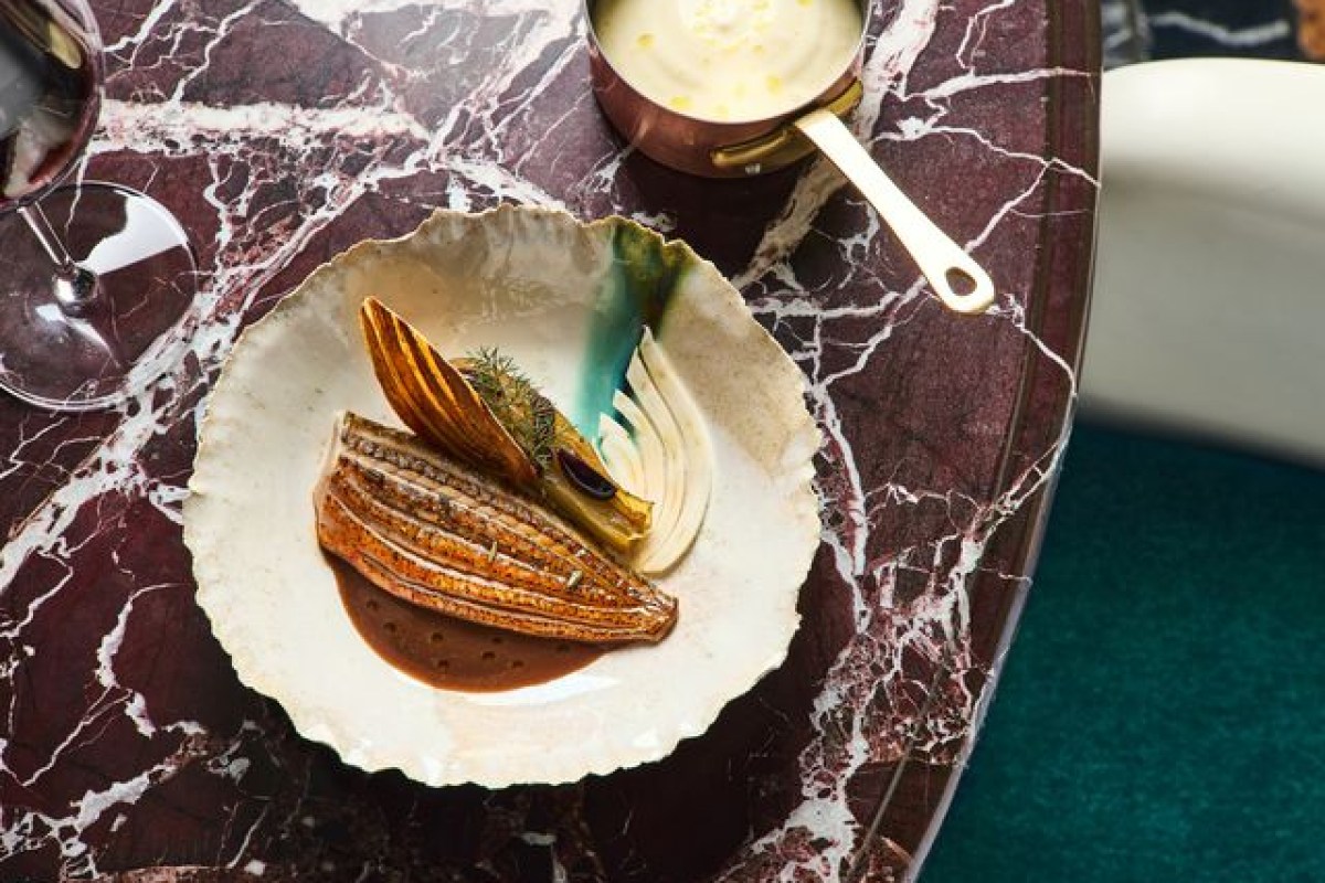 Plated fish dish with roasted vegetables and sauce on marbled table